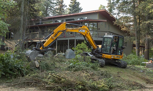 Excavator clearing brush and felled trees on a residential lot in Grand Rapids MI by Diversified Tree Service